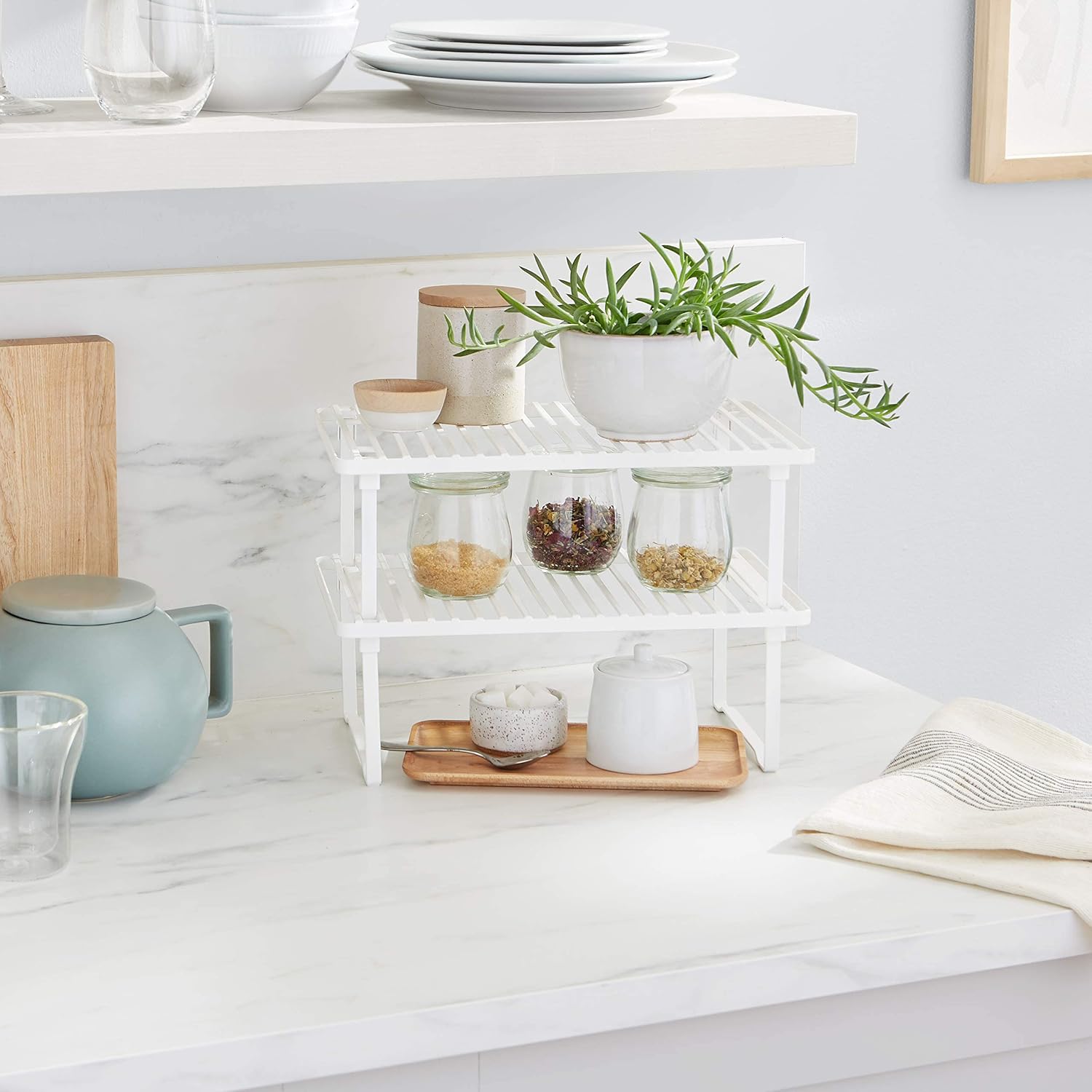 Set of two white stackable metal cabinet shelf risers — stacked risers used on a kitchen counter